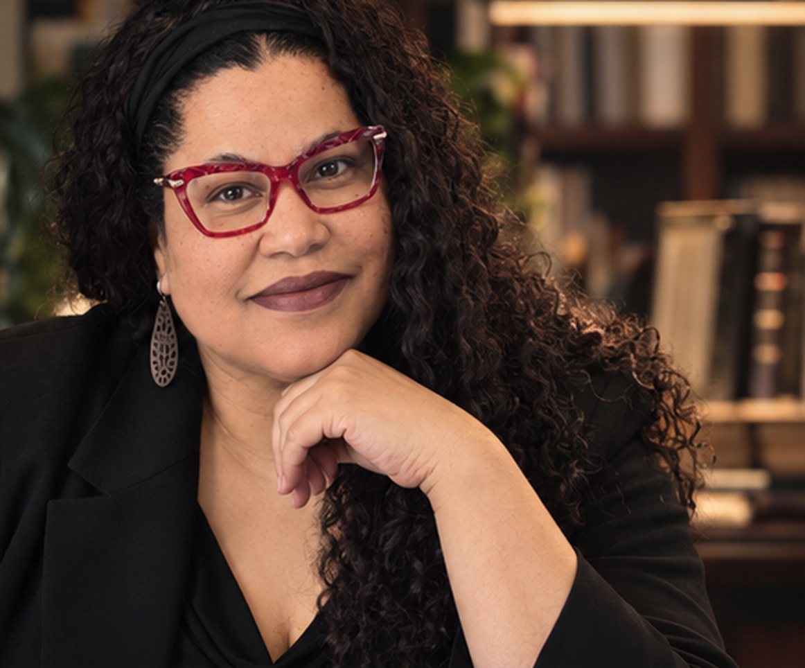 Jami Murphy in a black blazer and red glasses, seated in a library