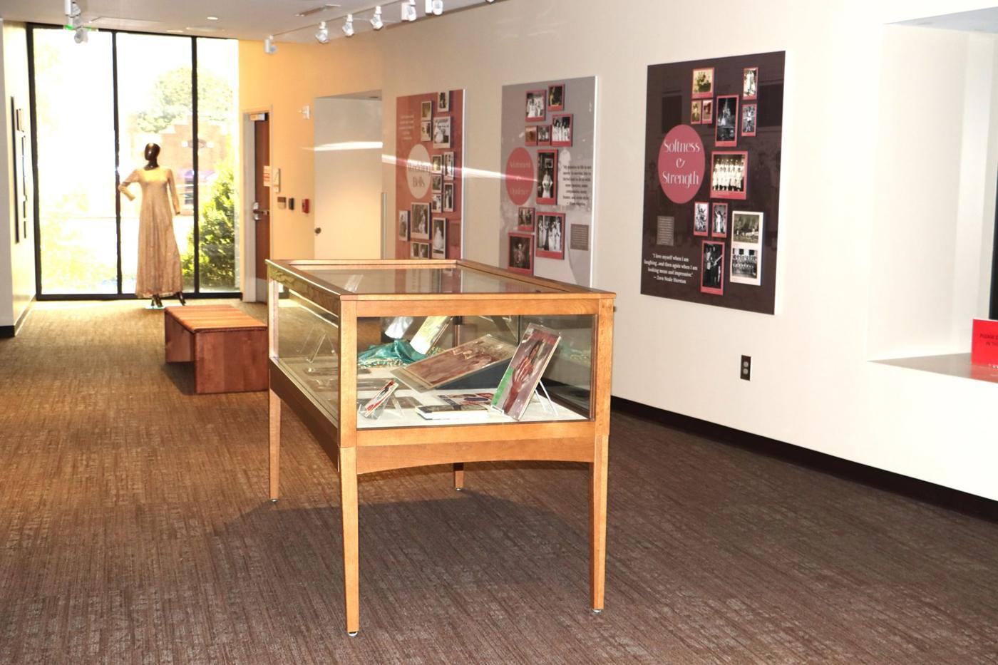 Gallery view of Softness Was Always Ours with framed photographs on dark panels and a central display case